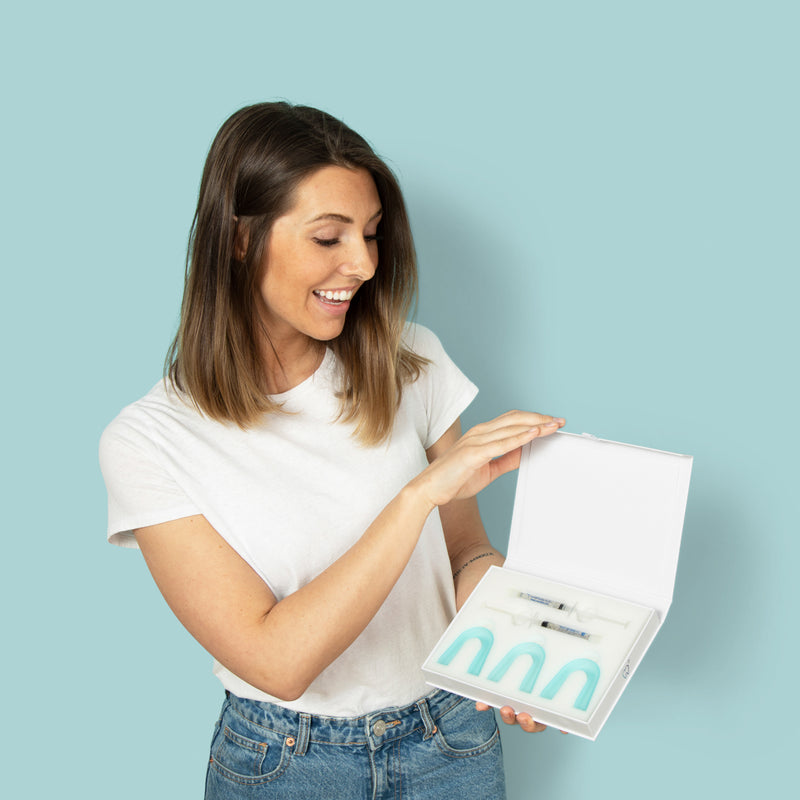 A smiling woman holding the CustMbite Smile Whitening Kit.
